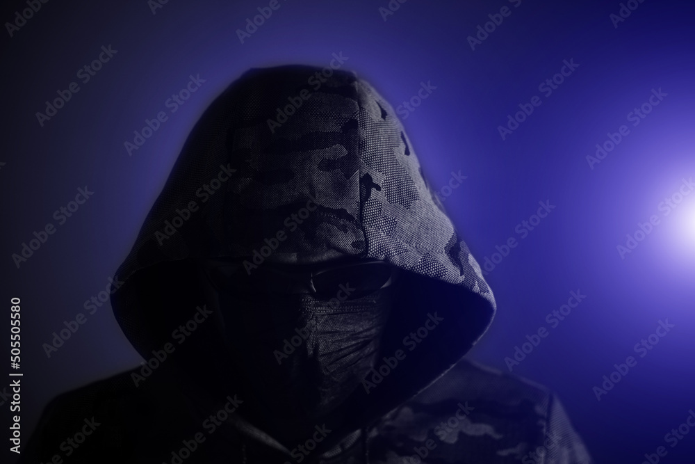 Φωτογραφία Stylish man in dark hoodie, black glasses and mask dark background in blue light, hacker, attacker and bandit