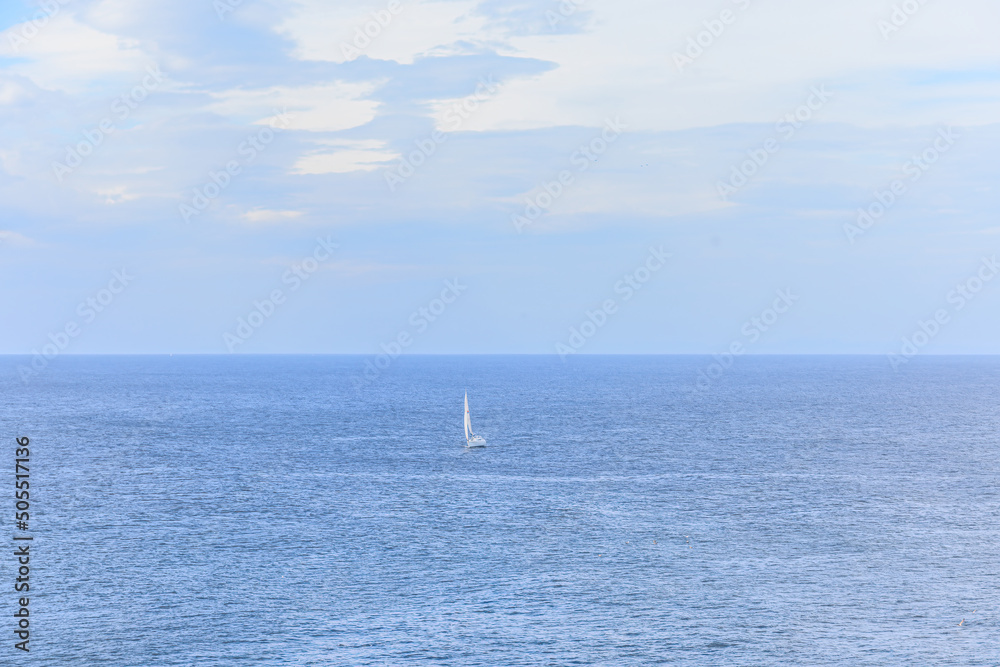 Fototapeta premium A scenic view of a sail boat on a majestic calm blue sea under a blue sky and some white clouds