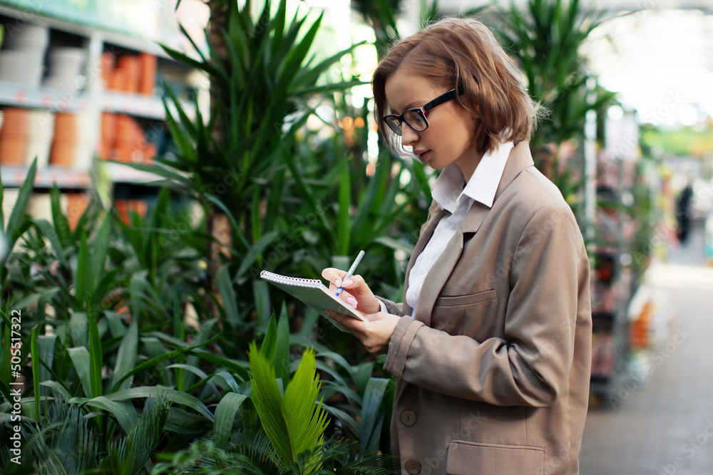Αυτοκόλλητο Young woman researcher at work in greenhouse, in business suit with notepad and pen in her hand