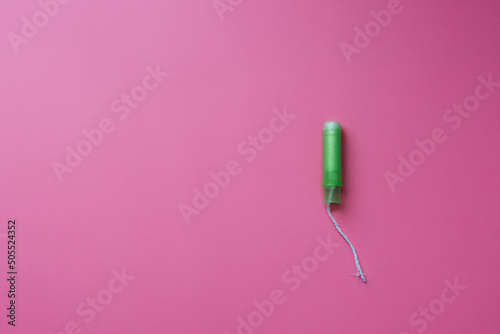Green tampon with plastic applicator on pink background, flat lay with copy space, female hygiene, menstruation or women period, monthly bleeding, gynecology and healthcare, feminine blog template photo