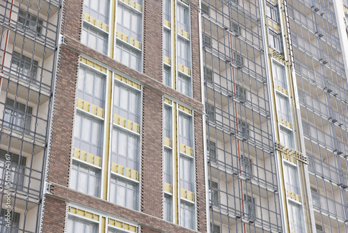 View of a modern residential building under construction. Installation of hinged facade on the buildings, installation of ceramic facade tiles on thermal insulation.