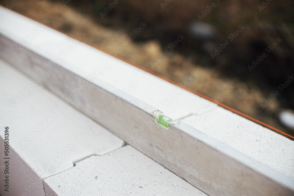 Water ruler on autoclaved aerated concrete blocks. Laying white blocks with measuring level close up. Masonry. Process of house building at construction site Water ruler on autoclaved aerated concrete blocks. Laying white blocks with measuring level close up. Masonry. Process of house building at construction site