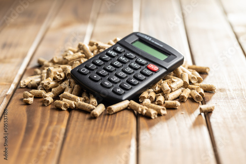 Wooden pellets and calculator, biofuel on wooden table. Ecologic fuel made from biomass. Renewable energy source.