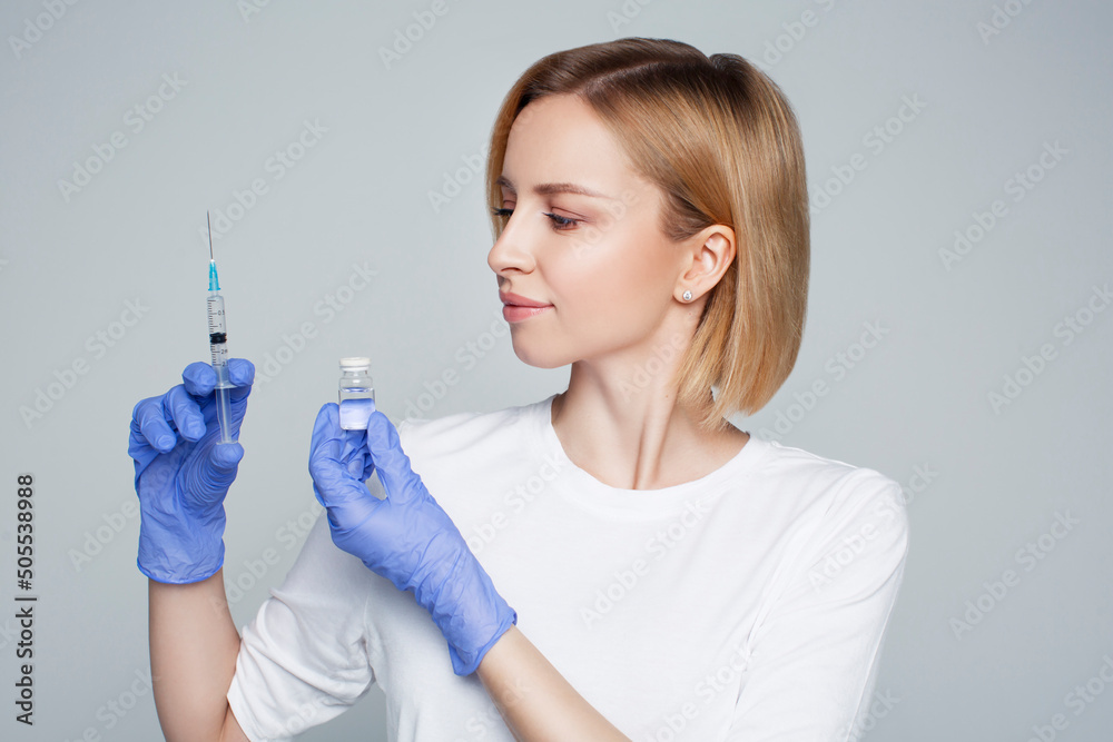 Blonde woman researcher holding liquid medicine drug and syringe in hands in blue gloves, disease vaccine injection. Treatment discover, beauty face injections, nurse or doctor, laboratory or hospital Blonde woman researcher holding liquid medicine drug and syringe in hands in blue gloves, disease vaccine injection. Treatment discover, beauty face injections, nurse or doctor, laboratory or hospital