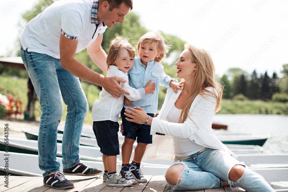 © Eva March - Happy four member family of mother, father and two boy kids hugging enjoying togetherness outdoors in park at sunny day. Young parents with boy twins sitting on wooden floor on pier. Family concept © Eva March - Happy four member family of mother, father and two boy kids hugging enjoying togetherness outdoors in park at sunny day. Young parents with boy twins sitting on wooden floor on pier. Family concept