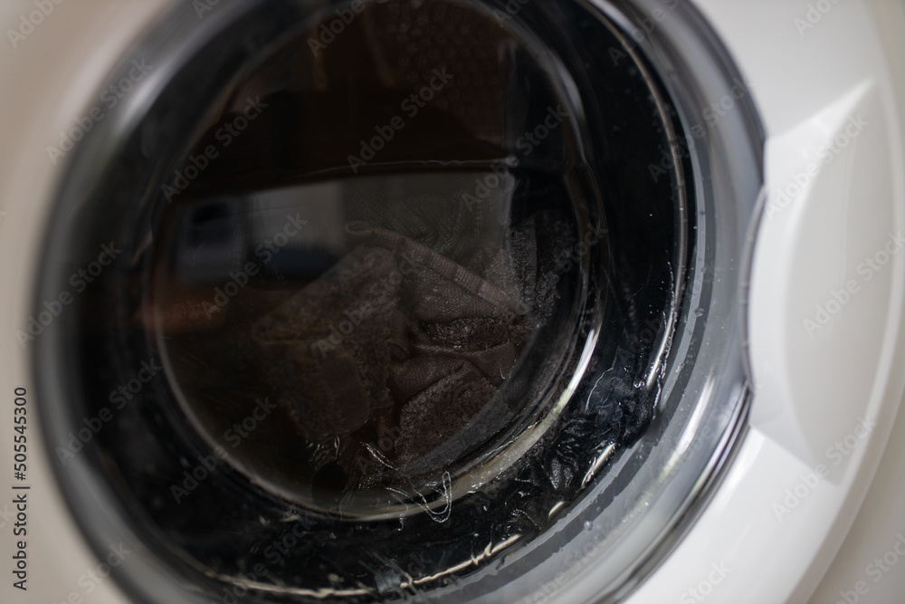 Washing machine door with rotating garments inside. focus in the center of dirty laundry and washing machine on the frame