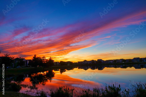 Beautiful pink, orange and blue sunset reflecting on a lake in a suburban neighborhood. © Joni