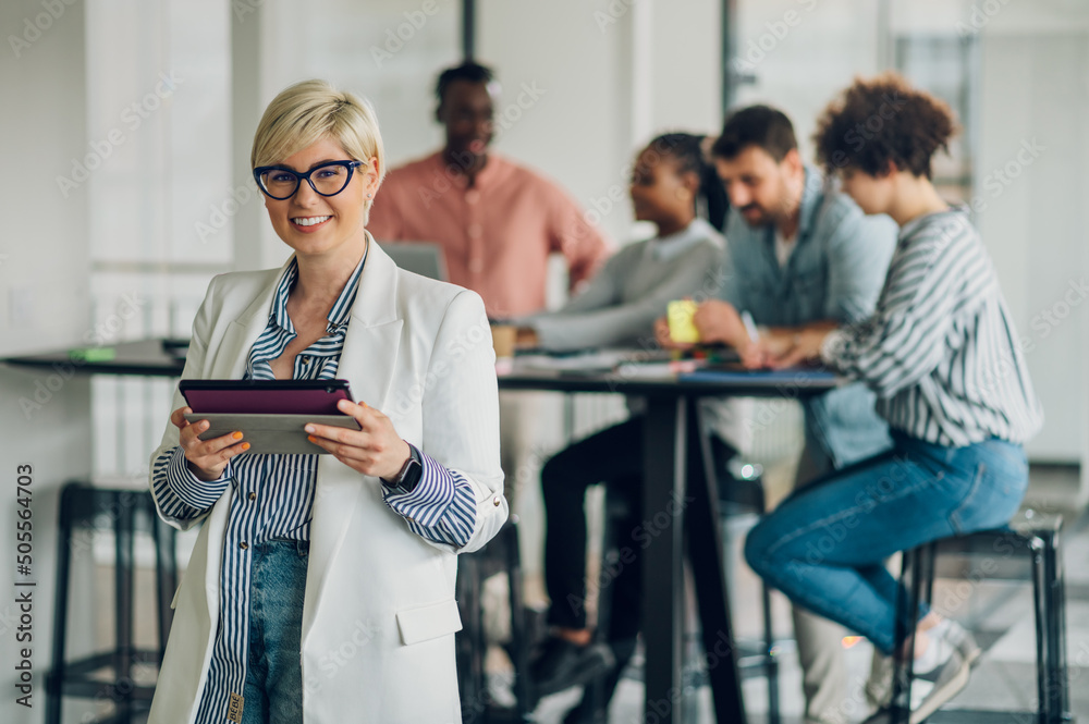 Portrait of a business woman standing in a office with colleagues in the back Portrait of a business woman standing in a office with colleagues in the back