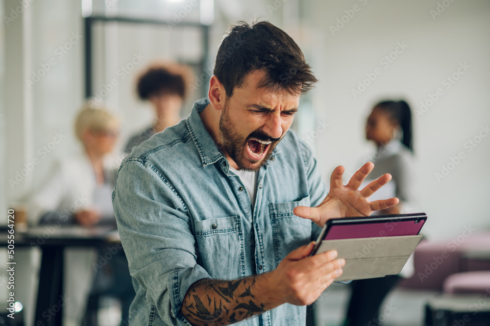 Stressed business man using tablet in the office with his team working in the back Stressed business man using tablet in the office with his team working in the back