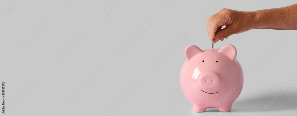 Hand of senior woman putting coin into piggy bank on light background with space for text - obrazy, fototapety, plakaty 
