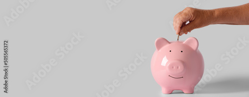 Hand of senior woman putting coin into piggy bank on light background with space for text photo