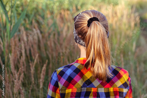 Defocus ponytail hairstyle. Teen or preteen girl walking on nature background and standing back. Little kid girl. Green meadow. Generation z. Autumn, summer. Bandana. Lifestyle. Sunny. Out of focus