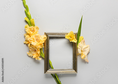 Empty picture frame and gladiolus flowers on grey background