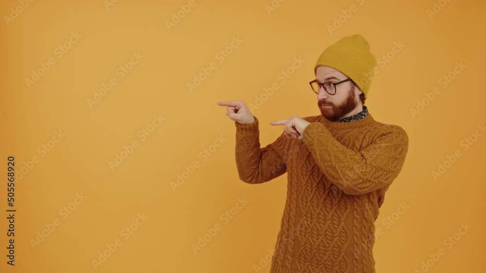 young bearded Caucasian man pointing left orange background medium shot studio shot advertisement concept. High quality 4k footage young bearded Caucasian man pointing left orange background medium shot studio shot advertisement concept. High quality 4k footage
