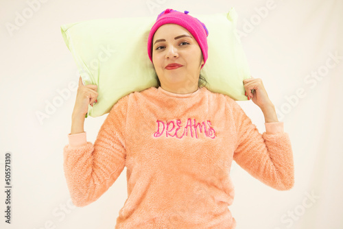 cute young asian white woman wearing pink pajamas, with a pillow and a night cap ready to sleep, smiling for a good day, on white background