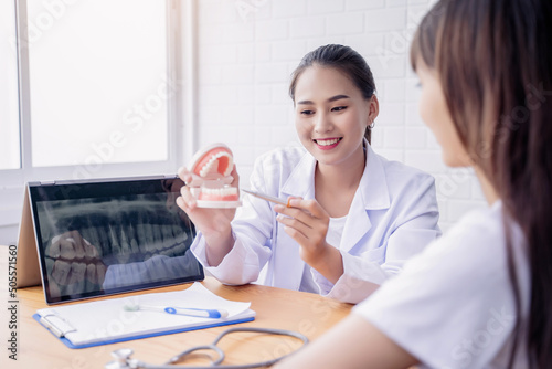 Fotografi Happy smiling Asian female dentist doctor examining teeth model diagnosing patie