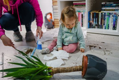 one caucasian baby girl making mess playing and mischief with bad behavior ripping paper towel and flower pot cruched on the floor naughty kid at home childhood and growing up misbehavior concept photo