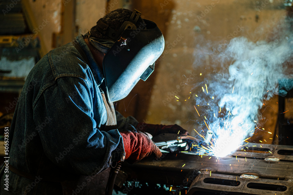 Welder Industrial works in an old workshop, holds a welding machine in his hand and welds metal structures at a factory. Welder Industrial works in an old workshop, holds a welding machine in his hand and welds metal structures at a factory.