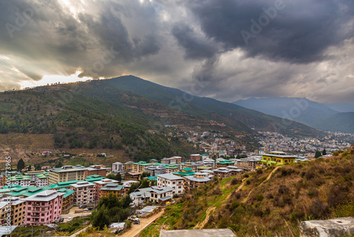 Thimphu, Bhutan - October 26, 2021: Aerial view cityscape of Bhutan capitol city. Top view with dramatic cloudy sky over the town. Largest city in Bhutan in a mountain valley. Houses with green roof © Holger