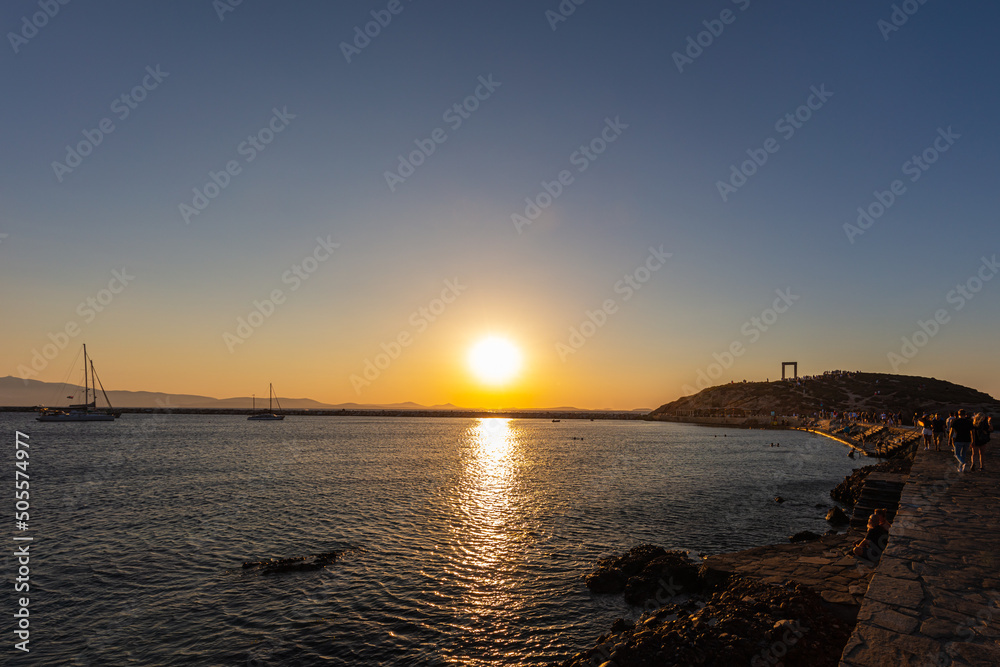 Sunset in Naxos Bay. The red and yellow glowing sun sinks on the horizon. Boats anchor and lie off the coast. Romantic scene in the Cyladen archipelago in the Aegean Sea. Sunset at the sea