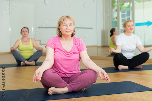 Mature woman making yoga meditation in lotus pose in fitness center