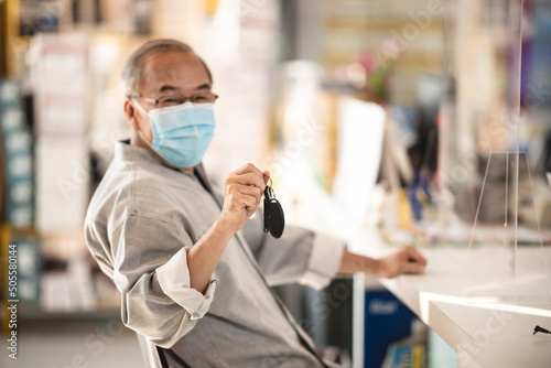 Young Asian sales man wearing covid-19 face protection mask while working on laptop giving car keys to senior customer during pandemic