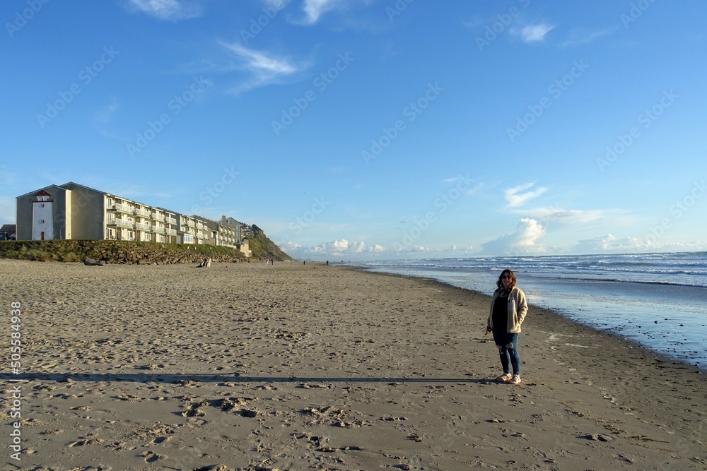 Φωτογραφία A woman standing and smiling posing for a photo with a beautiful view of the vast sandy beaches of Lincoln City, in central Oregon, United States, facing the pacific ocean
