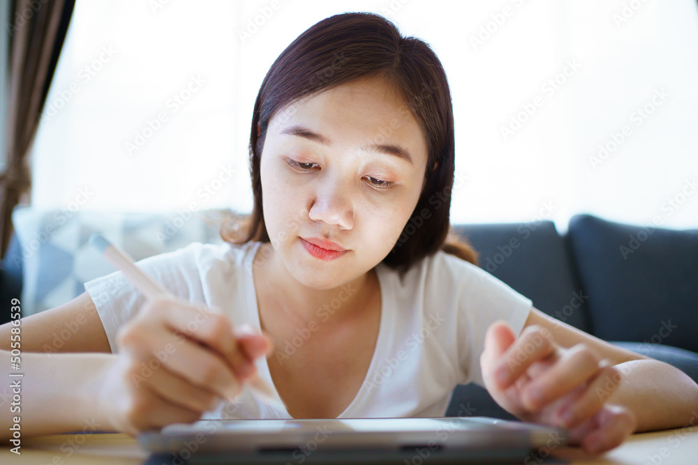 Happy Asian young woman relaxing in the living room and watching a contents and chatting with her friends and drawing an illustration on tablet. Woman enjoy watching video and drawing on tablet. Happy Asian young woman relaxing in the living room and watching a contents and chatting with her friends and drawing an illustration on tablet. Woman enjoy watching video and drawing on tablet.