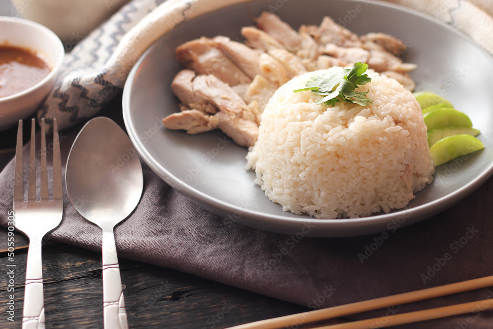Hainanese chicken rice served with dipping sauce and hot broth on a black wooden table.