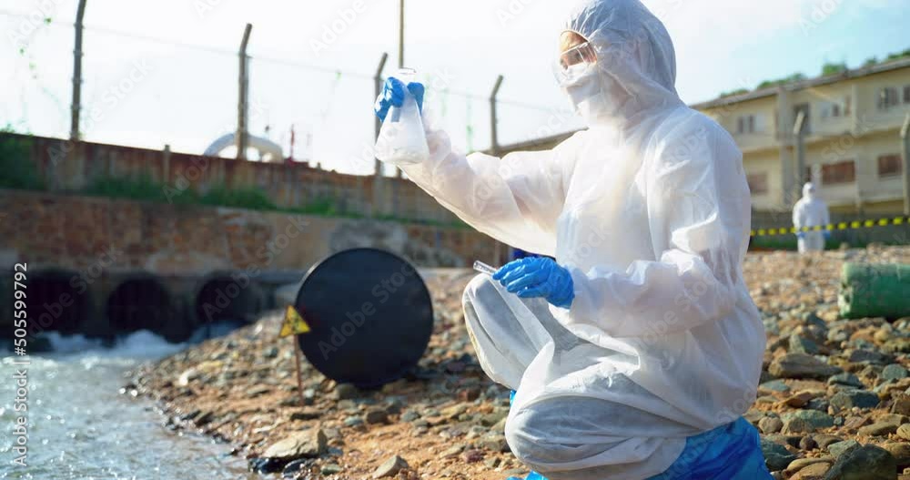 Asian women scientists in protective suits or Biologist collect sample of dirty water smelly and toxic water from factory took a sample of waste water for analysis. Asian women scientists in protective suits or Biologist collect sample of dirty water smelly and toxic water from factory took a sample of waste water for analysis.