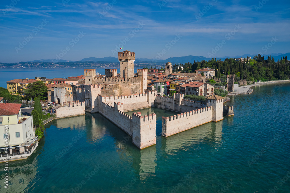 Scaligero Castle drone view. Italian castles Scaligero on the water. Flag of Italy on the towers of the castle on Lake Garda. Popular travel destination on Lake Garda in Italy. Sirmione top view.