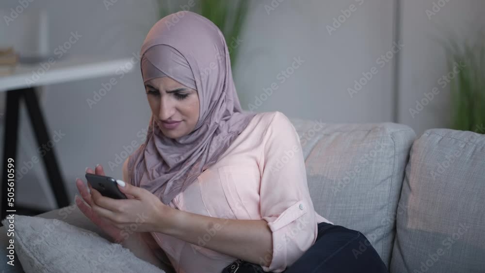 Phone problem. Low internet. Bad service. Impatient woman in hijab typing on lagging smartphone app annoyed with connection error on couch at home.