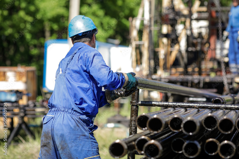 Oil and gas industry worker operates oil rig drill pipes on an oil well rig.