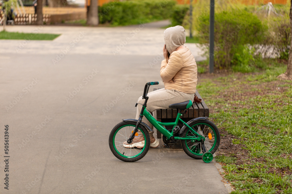 The girl is sitting on a bench with a bicycle. The girl is sitting on a bench with a bicycle.