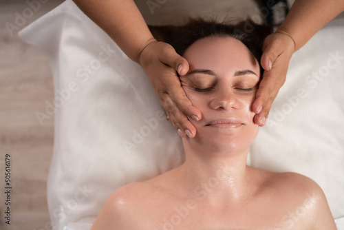 Young woman enjoying massage in spa salon  facial anti-aging massage in beauty salon  skin care