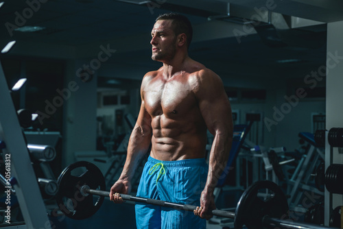 Muscular man doing biceps lifting barbell. Young man working out at crossfit gym. Athletic guy doing exercise.