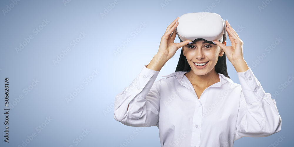 Virtual reality concept: smiled young woman in light shirt with VR glasses on her head on light blue background with place for your logo or text, mockup Virtual reality concept: smiled young woman in light shirt with VR glasses on her head on light blue background with place for your logo or text, mockup