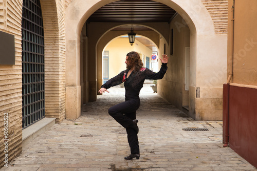 Young man with beard and long hair, wearing black transparent shirt with black polka dots and red roses, black pants and jacket, dancing flamenco in the city. Concept art, dance, culture, tradition.