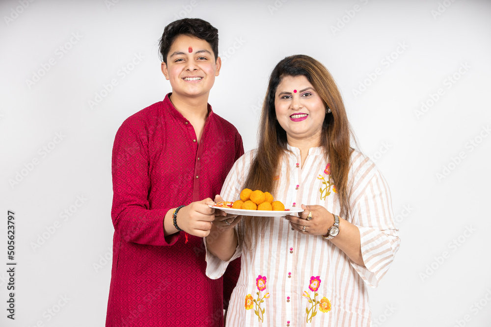 Φωτογραφία Portrait of happy young indian mother and son wearing traditional outfit holding plate full of laddu or laddoo sweets celebrating festival like diwali