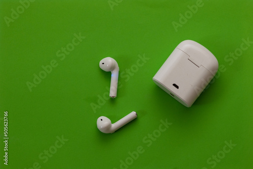 Small white wireless headphones near their holster - on a green background. top view