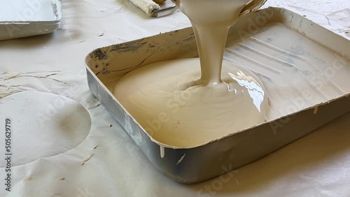 Pouring A Can of Ivory White Paint into an Aluminum Pan, Satisfying Pouring of Fresh Paint into Tray photo