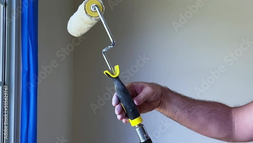 Painting Day, Male Painter Attaching a Paint Roller to a Pole in Room with White Walls photo