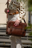 Part photo of a woman with a brown leather briefcase with antique and retro look. Outdoors photo