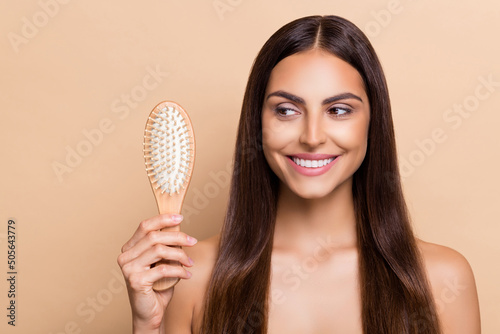 Portrait of attractive cheery girl holding brush strong shine curls daily care solution isolated over beige pastel color background