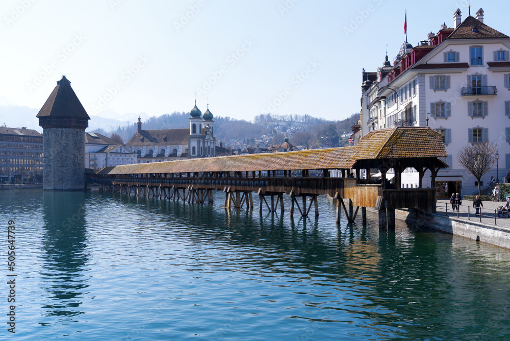Waterfront with famous water tower and covered wooden Chapel Bridge with Reuss River in the foreground at the old town of Luzern on a spring day. Photo taken March 23rd, 2022, Lucerne, Switzerland.