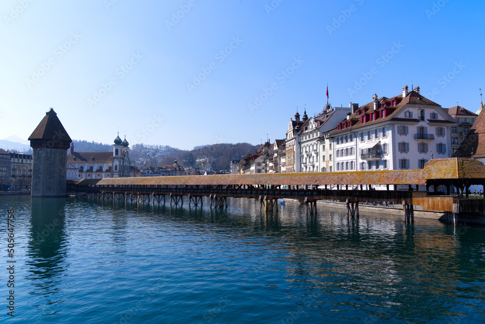 Waterfront with famous covered wooden Chapel Bridge with Reuss River in the foreground at the old town of Luzern on a spring day. Photo taken March 23rd, 2022, Lucerne, Switzerland.