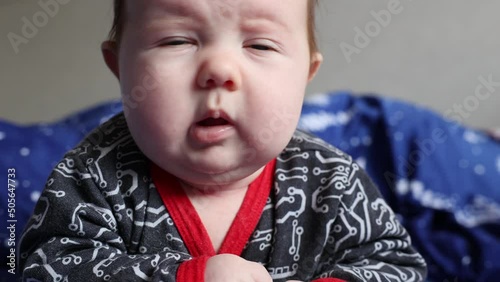Little newborn baby boy lies on a bed on his front looking at camera. Portrait of a lonely child trying to hold his head up. New life, parenthood, raising a child and milestone concept.