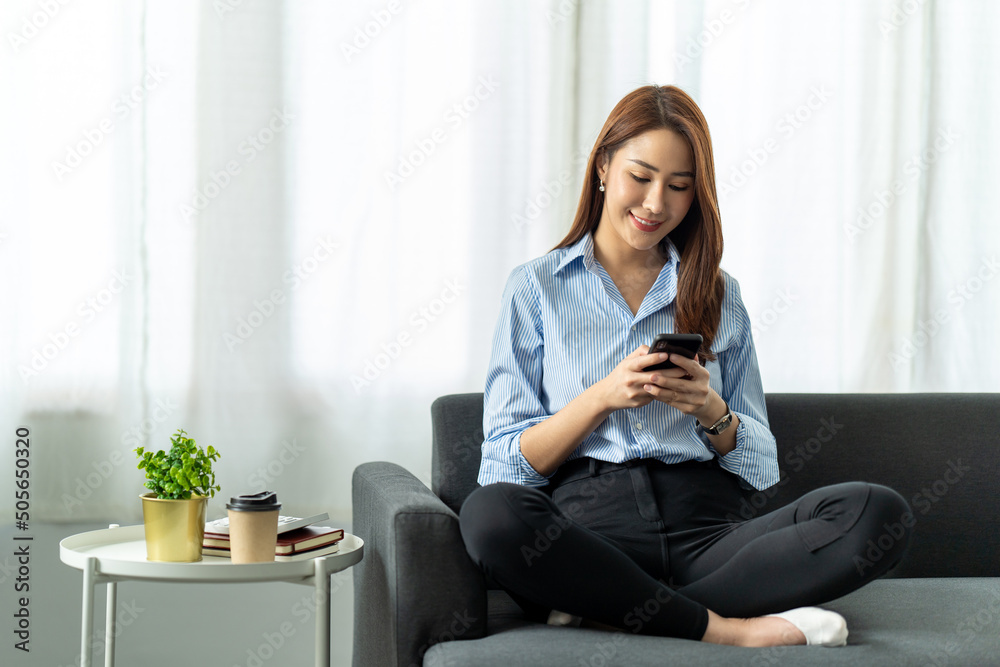 Smiling young asian woman using mobile phone while sitting on a couch at home, Technology and communication concept. Smiling young asian woman using mobile phone while sitting on a couch at home, Technology and communication concept.