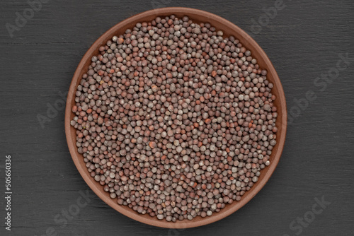 Mustard seeds in clay plate on black wooden background. Macro. Vegetarian food concept