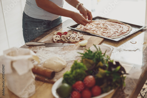 A woman prepares homemade pizza with vegetables and mushrooms in the kitchen. Pizza cooking process